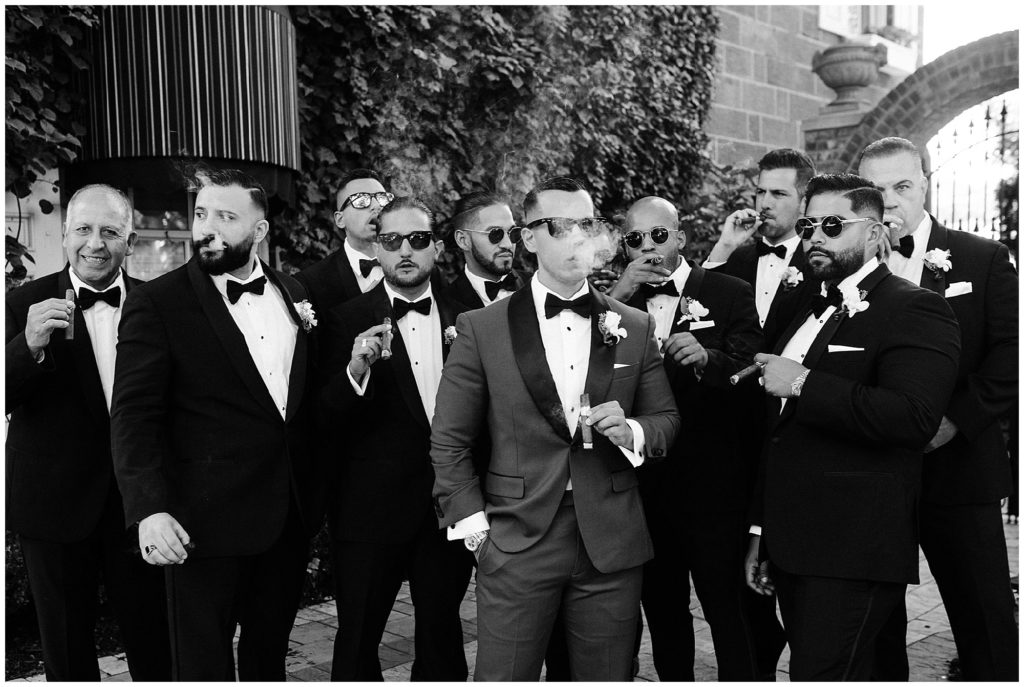 Black and white photo of the Groom and his Groomsmen smoking cigars on his wedding day at the Brownstone.  Renee Ash Photography