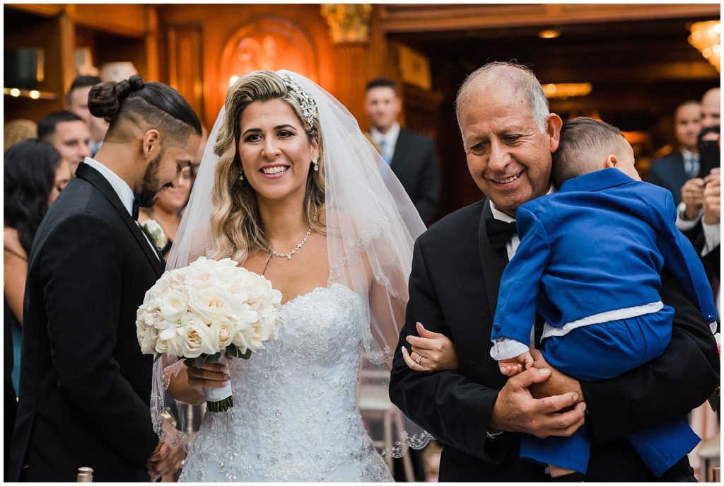 Bride's father and toddler son walking her down the aisle during their ceremony at the Grand Conservatory at the Brownstone.  Renee Ash Photography