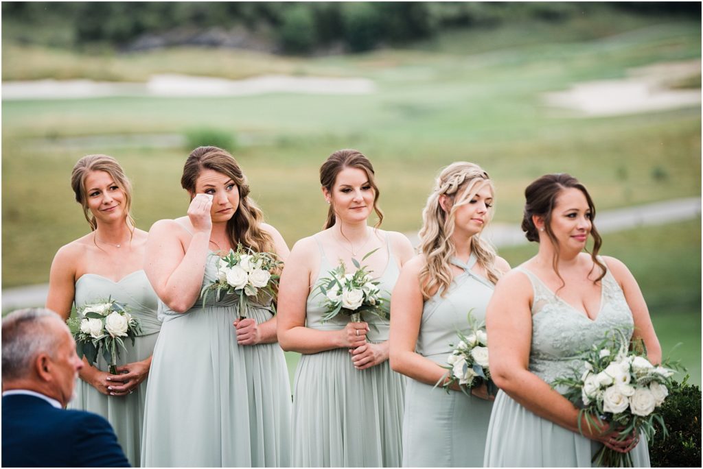 Bridesmaids in sage green dresses standing during the ceremony with the golf course view. Ballyowen at Crystal Springs summer wedding. Renee Ash Photography, Hamburg NJ 