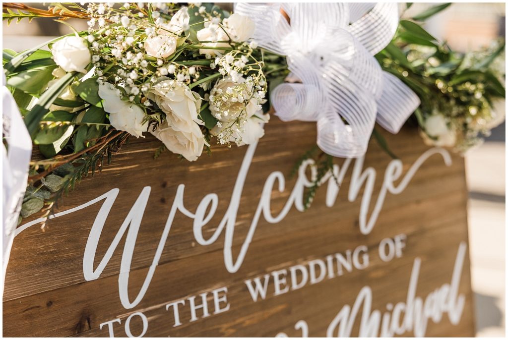 wooden welcome sign hand caligraphed with white roses and eucalyptus floral swag. 