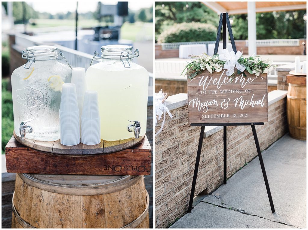 Water and lemonade ceremony welcome station with a wooden welcome sign hand caligraphed with white roses and eucalyptus floral swag.