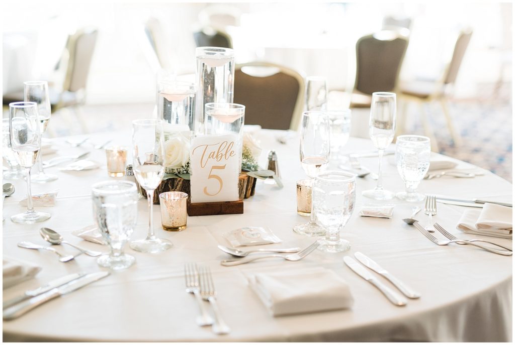 Three floating candle centerpiece with wood round and white roses. SImple white and gold acrylic table number sign. Reception decor at The Club at Picatinny. Renee Ash Photography