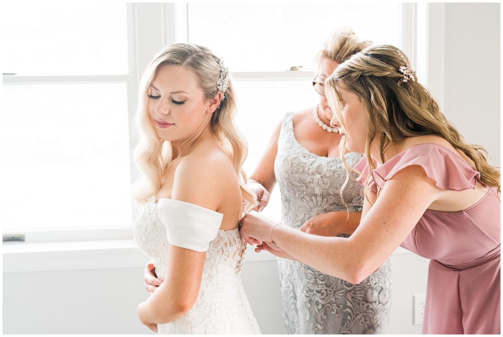 Bride getting into her dress with her mom and sister helping her at The Club at Picatinny.  New Jersey wedding venue. Renee Ash Photography