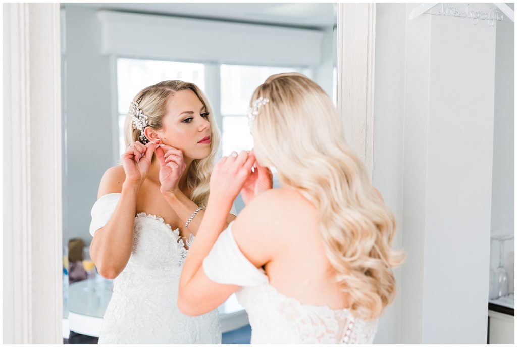 Bride getting ready putting in her earrings in front of  a mirror in the bridal suite  at The Club at Picatinny.  New Jersey wedding venue. Renee Ash Photography