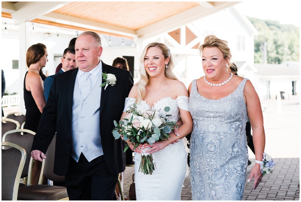Bride walking down the aisle escorted by her mom and dad at The Club at Picatinny.  Pronovias wedding dress.  White rose and Eucalyptus bouquet. Renee Ash Photography