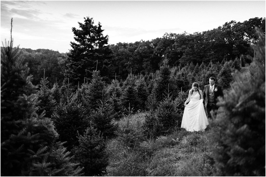 Black and white photo of the bride and groom walking through pine trees at Emmerich Tree Farm Wedding warwick NY 