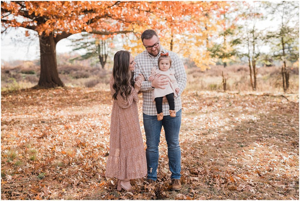 Fall Family of three first birthday pictures with a one year old girl in the fall leaves in October. Central Park of Morris Plains NJ Family photographer Renee Ash Photography