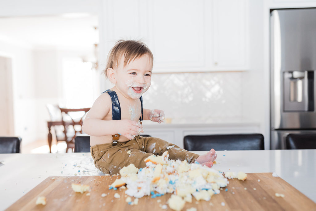 The why behind the photographs.boy's first birthday photoshoot at home in the kitchen with a homemade cake. Sitting on the kitchen island for his cake smash wearing suspenders and khakis. Vernon NJ in home photoshoot. Renee Ash Photography 