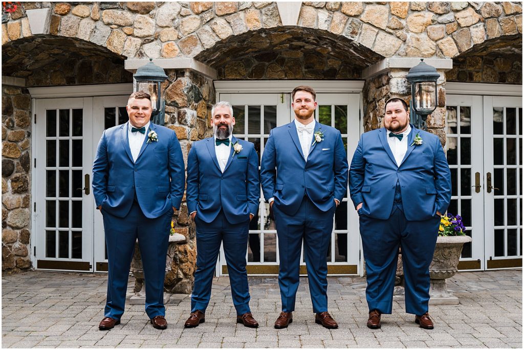 Groomsmen in navy blue suits with green bowties.  In the courtyard at The Olde Mill Inn Wedding Venue in Northern NJ. by Renee Ash Photography 