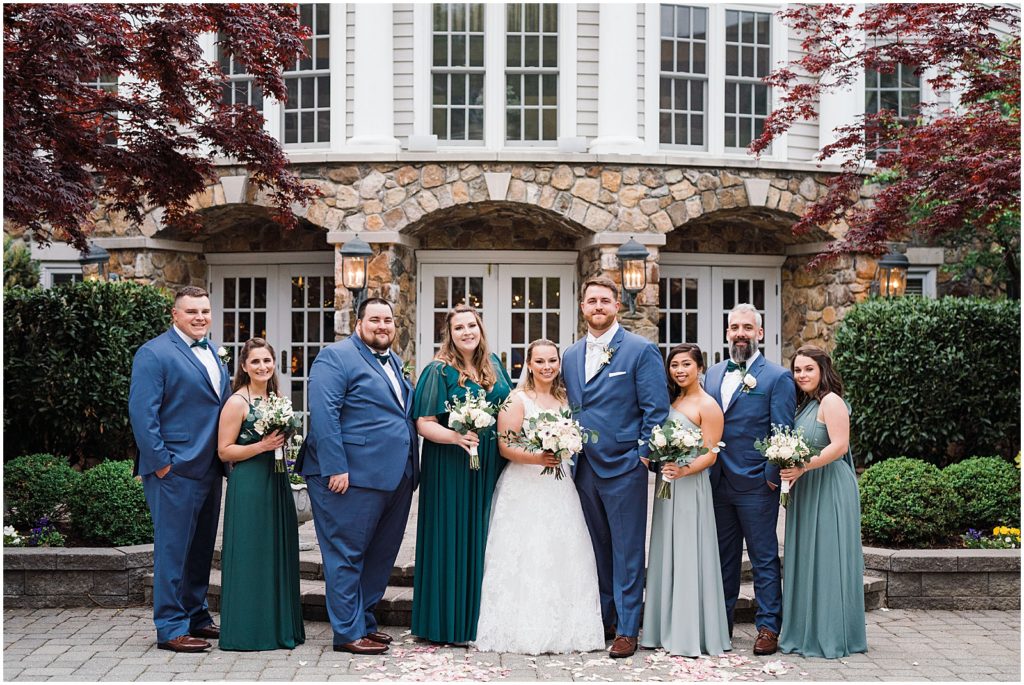 Bridal Party photos in the courtyard ceremony space of The Olde Mill Inn Wedding Venue in Northern NJ. Navy blue suits and mix and match green bridesmaid gowns. photos by Renee Ash Photography 