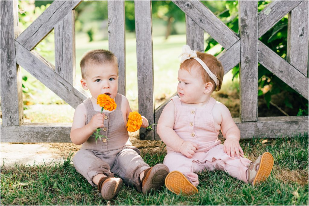 Cousins sitting next to one another in front of a garden gate holding an orange marigold flower.
At the Mohonk Mountain house in New York Renee Ash Photography