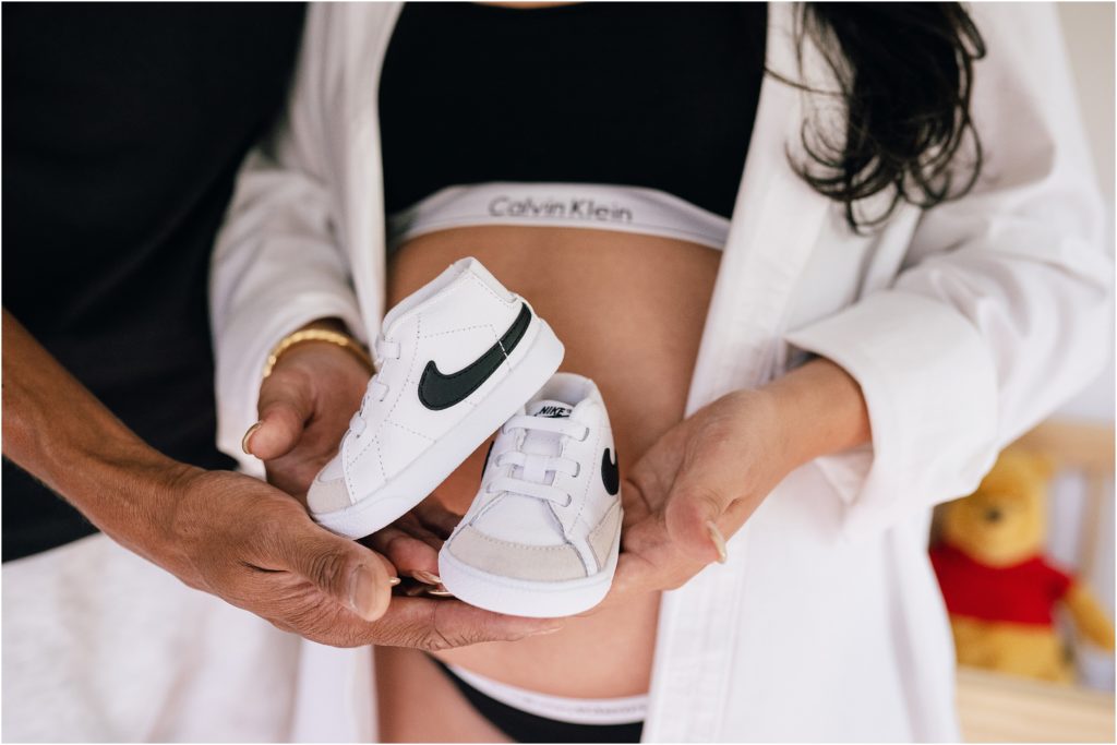 Baby's first nikes. White nike baby sneakers in mom and dad's hands. In home maternity pictures NJ.