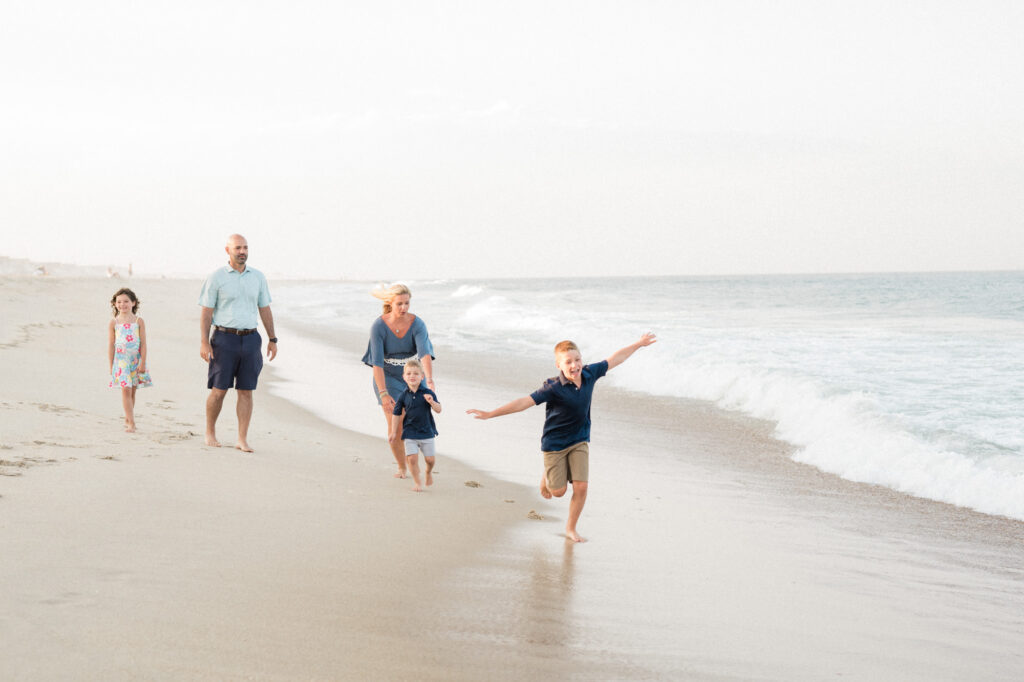 Summer Photo Session Ideas at the new jersey shore with family. Family running down the beach playing in the waves at sunset. 