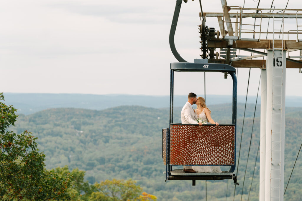 Bride and Groom ride the ski lift gondola from their wedding ceremony on top of the mountain with a view at a Late September Mountain Creek Wedding at Red Tail Lodge. 