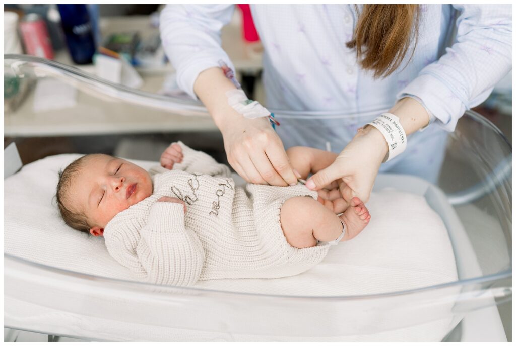 Mom changing baby's outfit into a hello world sweater of  Baby boy just 24 hours old in the hospital after delivery at Morristown Medical Center during baby's first photo shoot with Fresh 48 Newborn Photographer renee Ash Photography