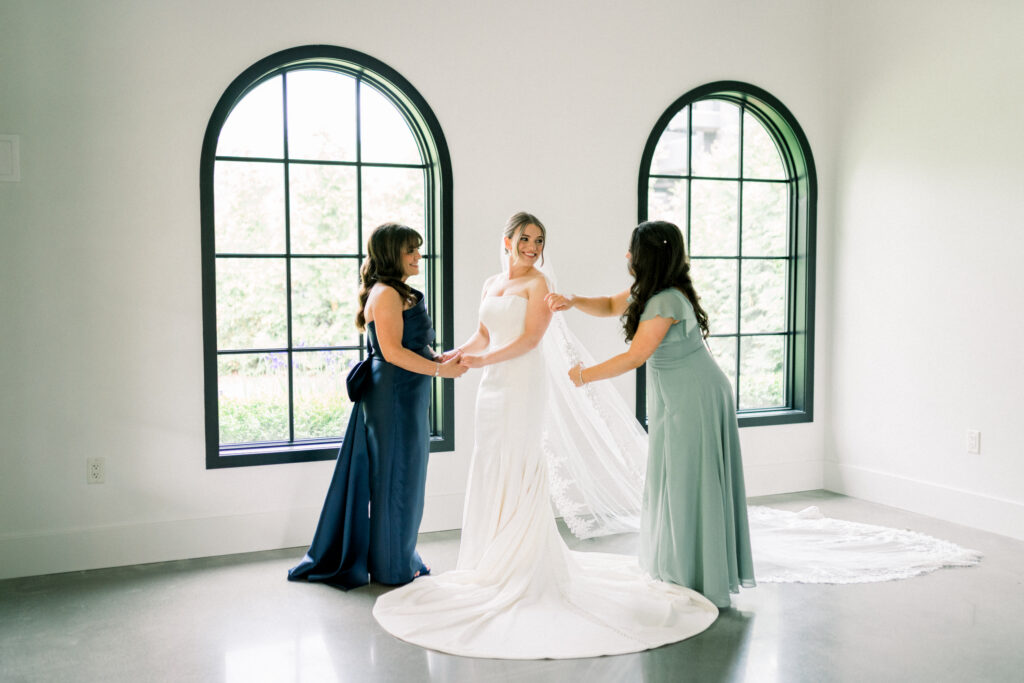 Wedding photography timeline tips. Morning of the wedding day bride getting into the wedding dress with the help of her mom and sister at Perona Farms wedding venue in north new jersey