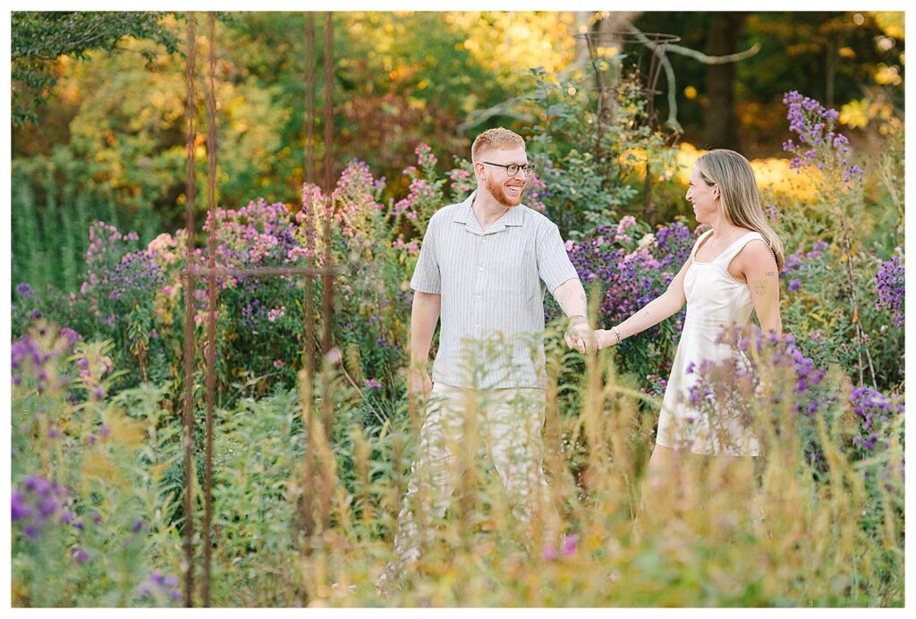 Candid engagement photography at New Jersey Botanical Gardens with a fun loving couple dancing in warm sunset light surrounded by flowers.